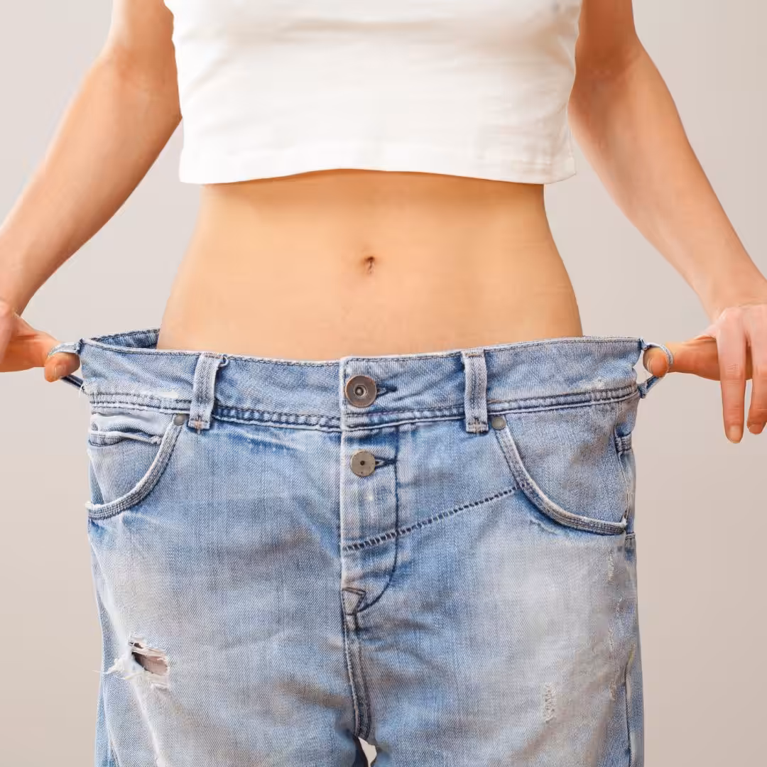 Woman wearing jeans too big for her and holding out the sides to show size difference