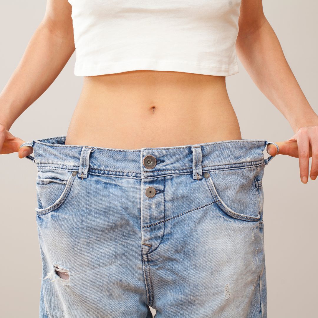 Woman wearing jeans too big for her and holding out the sides to show size difference 